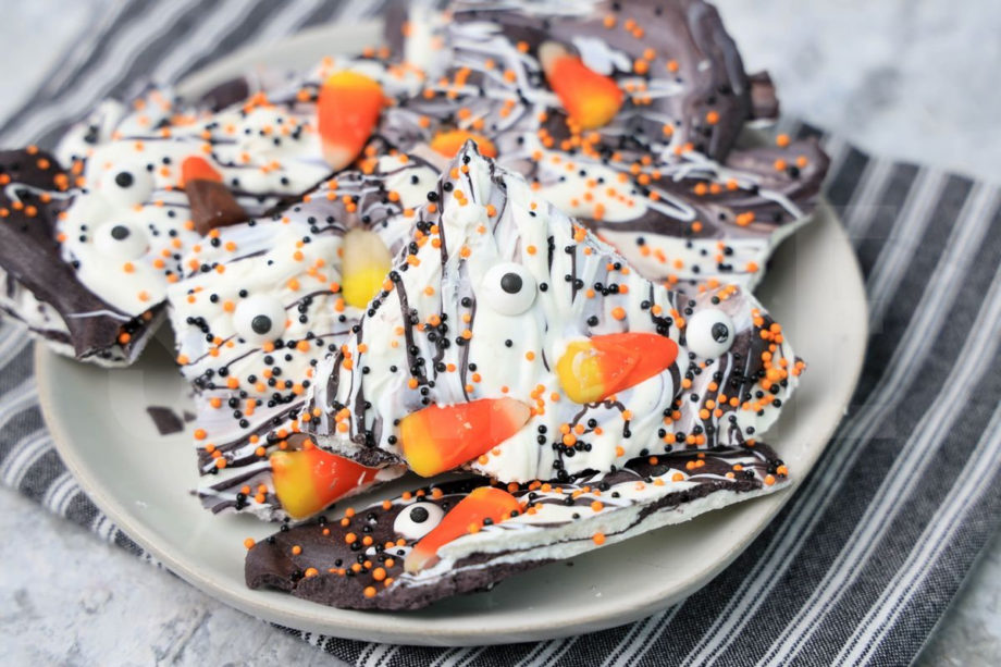 The Vintage Halloween Candy Bark comes on a white plate with a gray striped napkin on a marble backdrop.