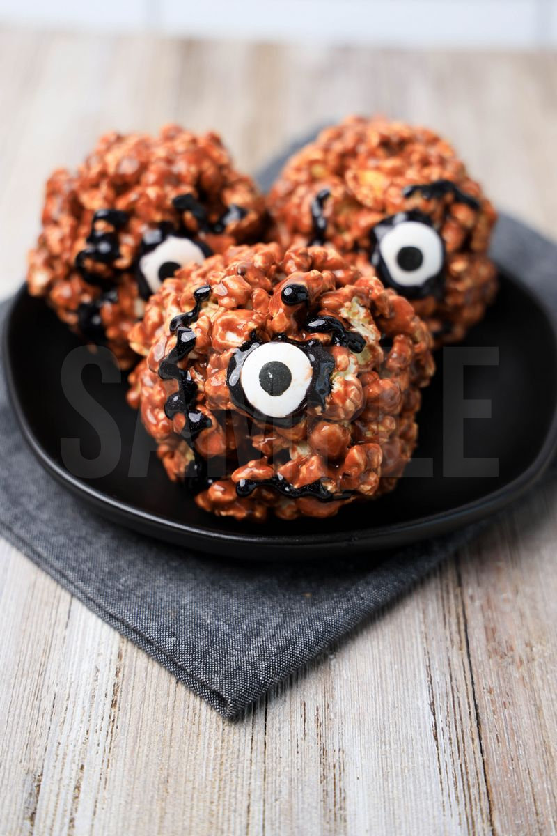 The Hocus Pocus Book Of Spells Popcorn Balls comes on a black plate with a denim napkin on a rustic wood backdrop.