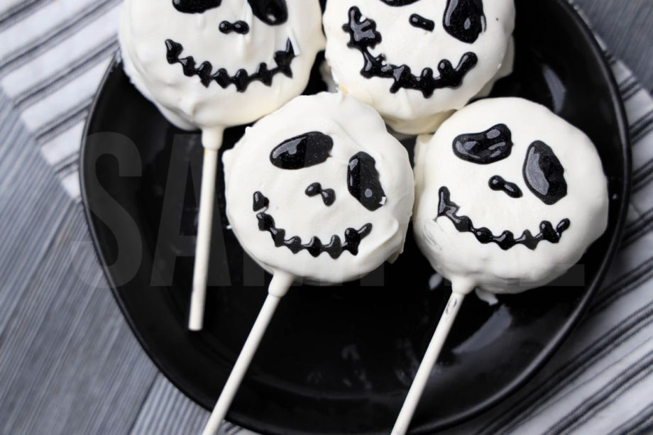 The Nightmare Before Christmas Rice Krispy Pops comes a black plate with a white striped napkin on a gray wood backdrop.