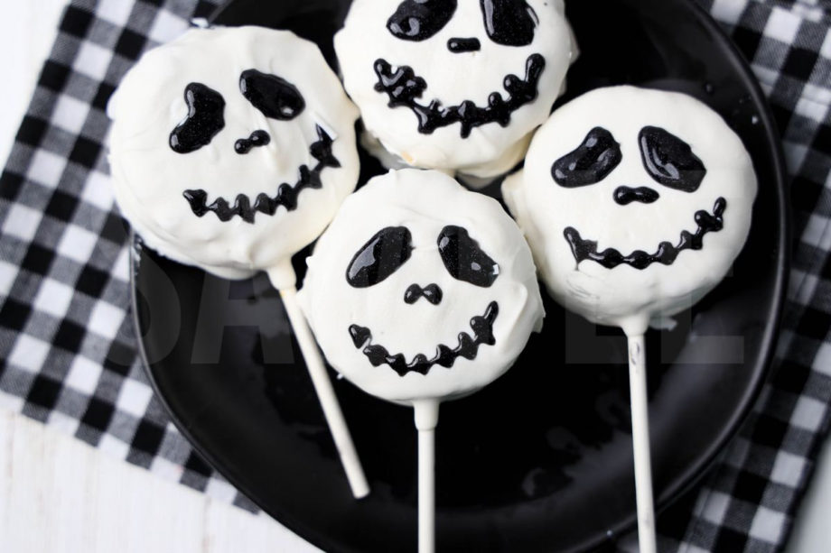 The Nightmare Before Christmas Rice Krispy Pops comes a black plate with a plaid napkin on a white wood backdrop.