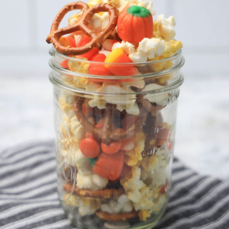 The Fall Snack Mix comes in a mason jar with a gray striped napkin on a marble backdrop.