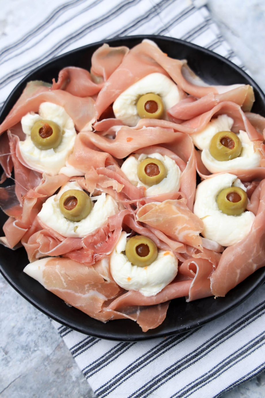 The Prosciutto Eyeballs comes on a black plate with a white striped napkin on a marble backdrop.
