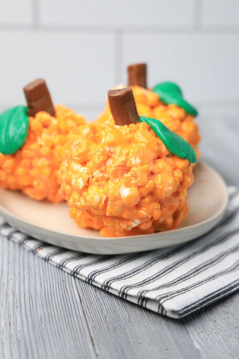 The Pumpkin Popcorn Balls comes on a white plate with a white striped napkin on a gray wood backdrop.