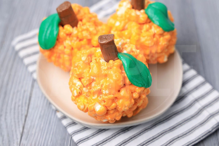 The Pumpkin Popcorn Balls comes on a white plate with a white striped napkin on a gray wood backdrop.