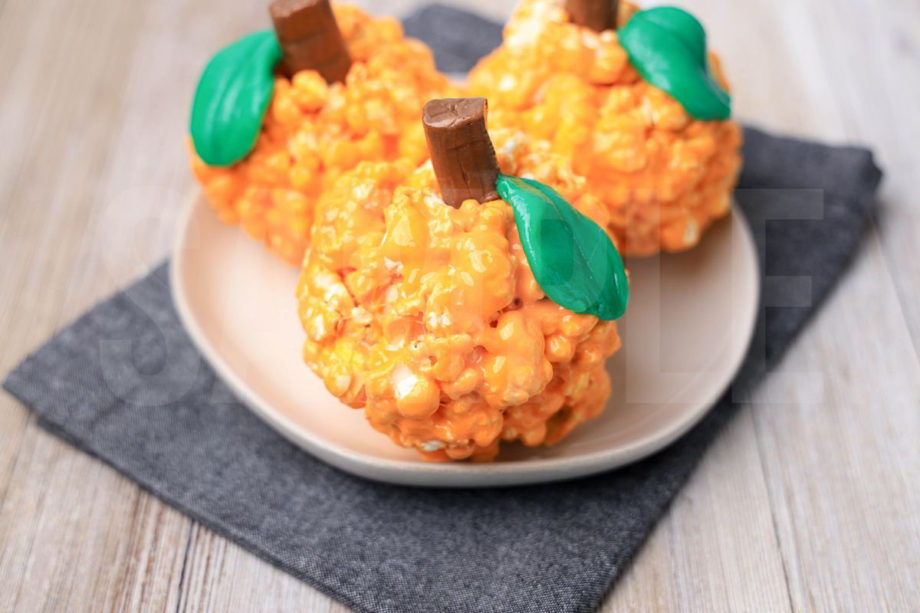 The Pumpkin Popcorn Balls comes on a white plate with a denim napkin on a rustic wood backdrop.