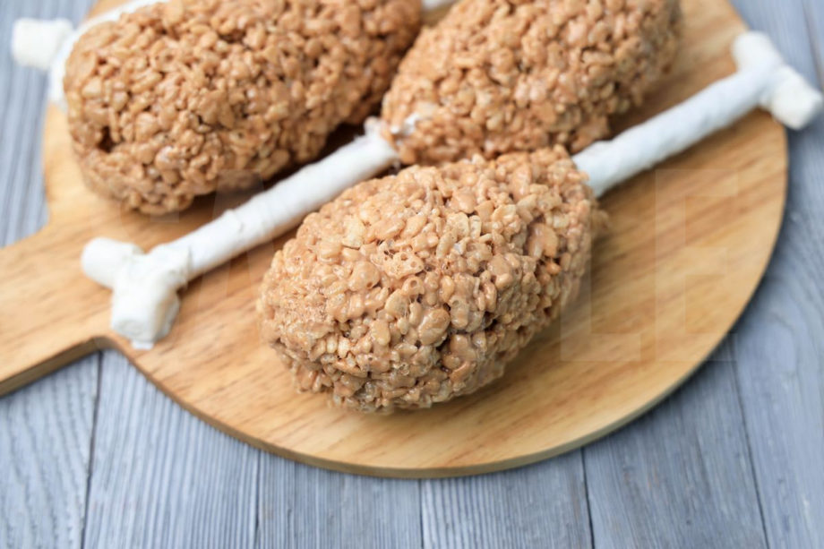 The Turkey Leg Rice Krispies Treats comes on a wood board with a white striped napkin on a gray wood backdrop.