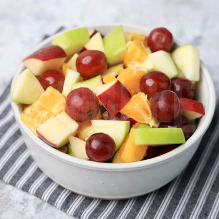 The Fall Fruit Salad comes in a white bowl with a gray striped napkin on a marble wood backdrop.