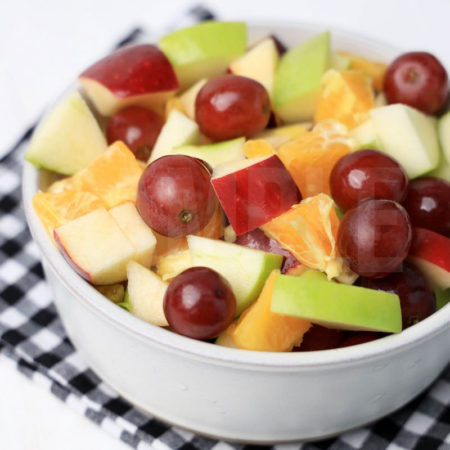 The Fall Fruit Salad comes in a white bowl with a plaid napkin on a white wood backdrop.