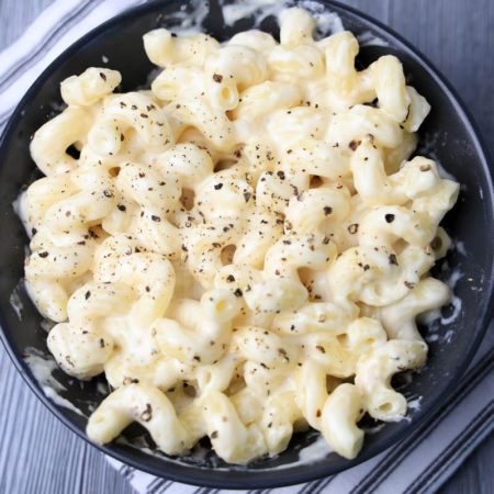 The Pepper Jack Mac and Cheese Cavatappi comes in a white bowl with a white striped napkin on a gray wood backdrop.