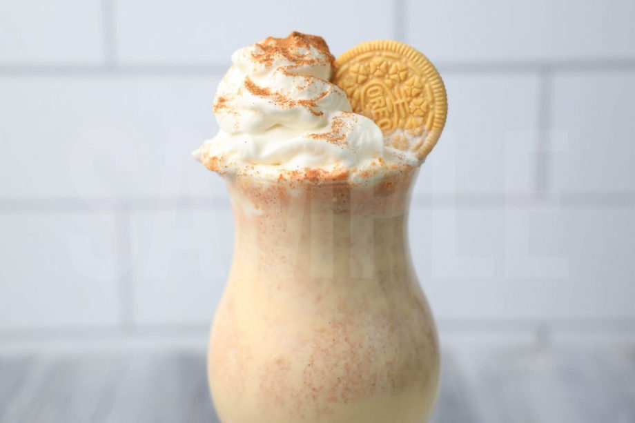 The Pumpkin Spiced Oreo Shake comes in a glass with a white striped napkin on a gray wood backdrop.