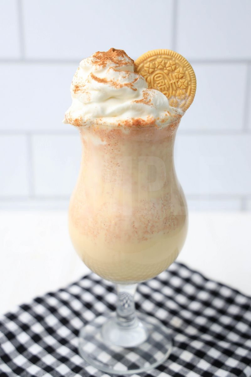 The Pumpkin Spiced Oreo Shake comes in a glass with a plaid napkin on a white wood backdrop.