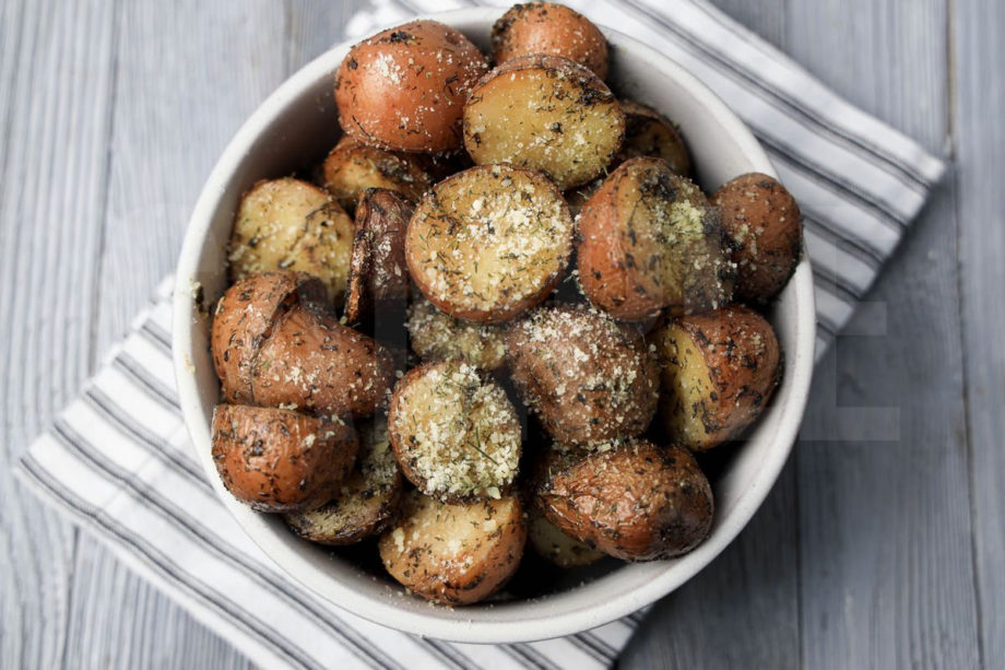 The Slow Cooker Roasted Parmesan Herb Potatoes comes in a white bowl with a white striped napkin on a gray wood backdrop.