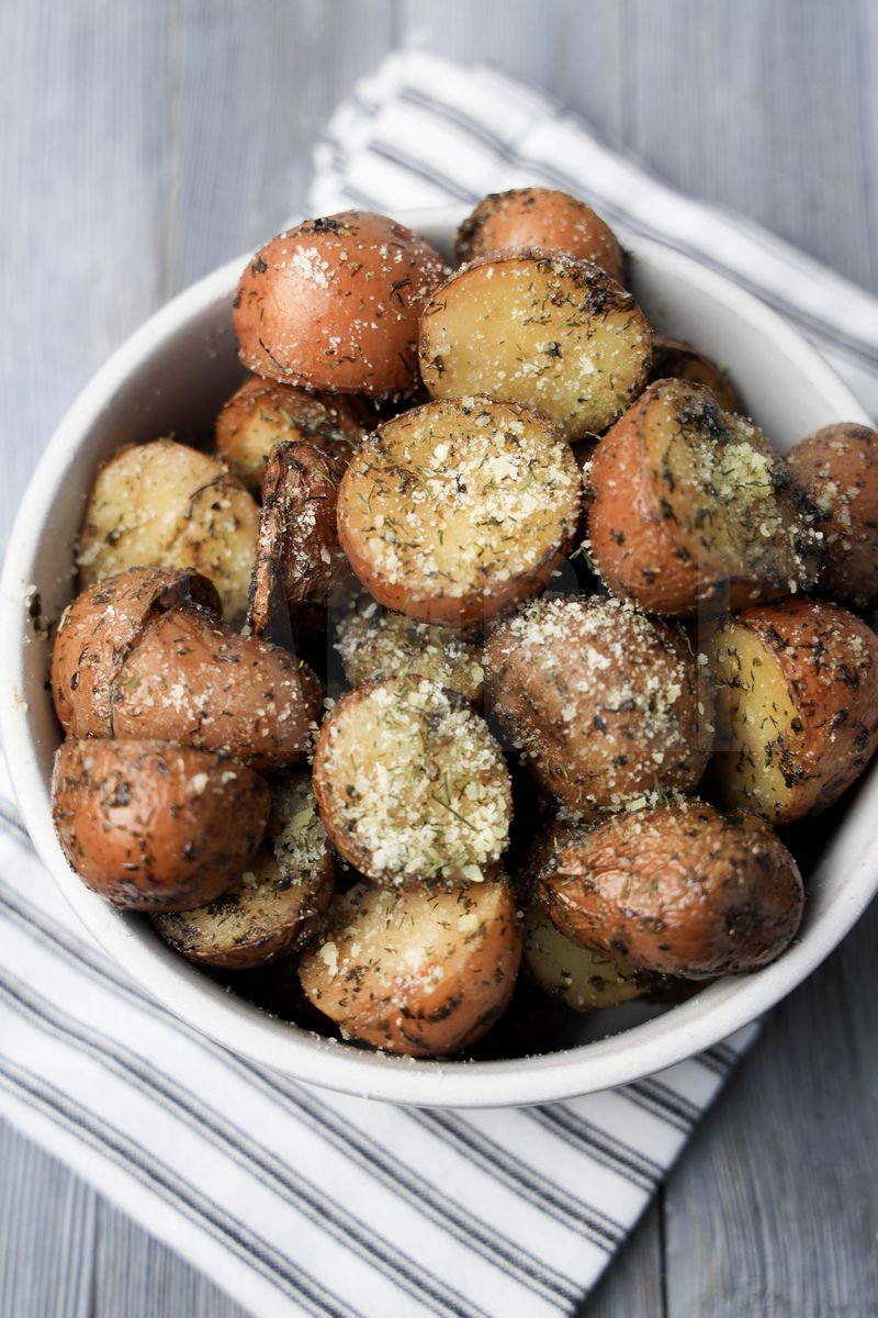 The Slow Cooker Roasted Parmesan Herb Potatoes comes in a white bowl with a white striped napkin on a gray wood backdrop.