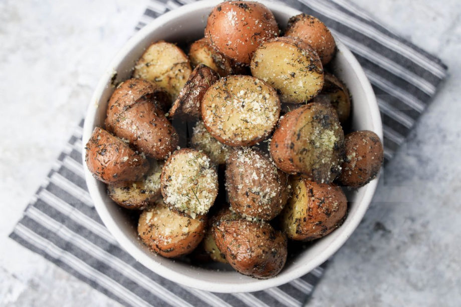 The Slow Cooker Roasted Parmesan Herb Potatoes comes in a white bowl with a gray striped napkin on a marble backdrop.