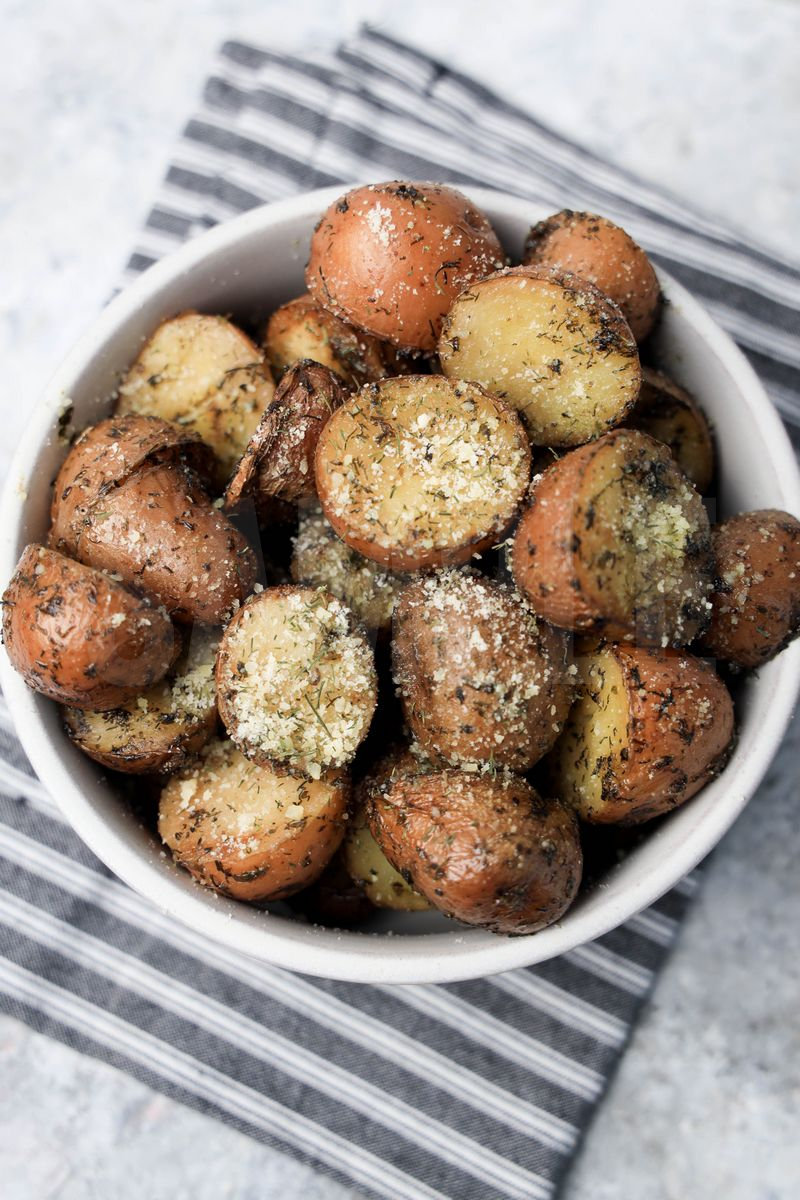 The Slow Cooker Roasted Parmesan Herb Potatoes comes in a white bowl with a gray striped napkin on a marble backdrop.