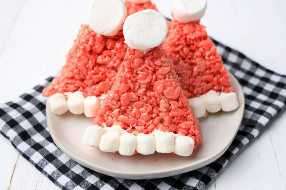 The Santa Hat Rice Krispies Treats comes on a white plate with a plaid napkin on a white wood backdrop.