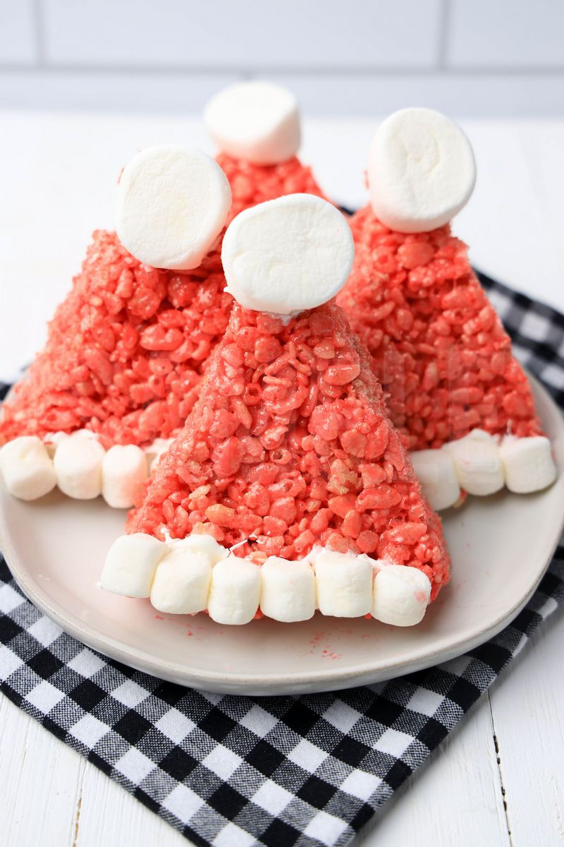 The Santa Hat Rice Krispies Treats comes on a white plate with a plaid napkin on a white wood backdrop.