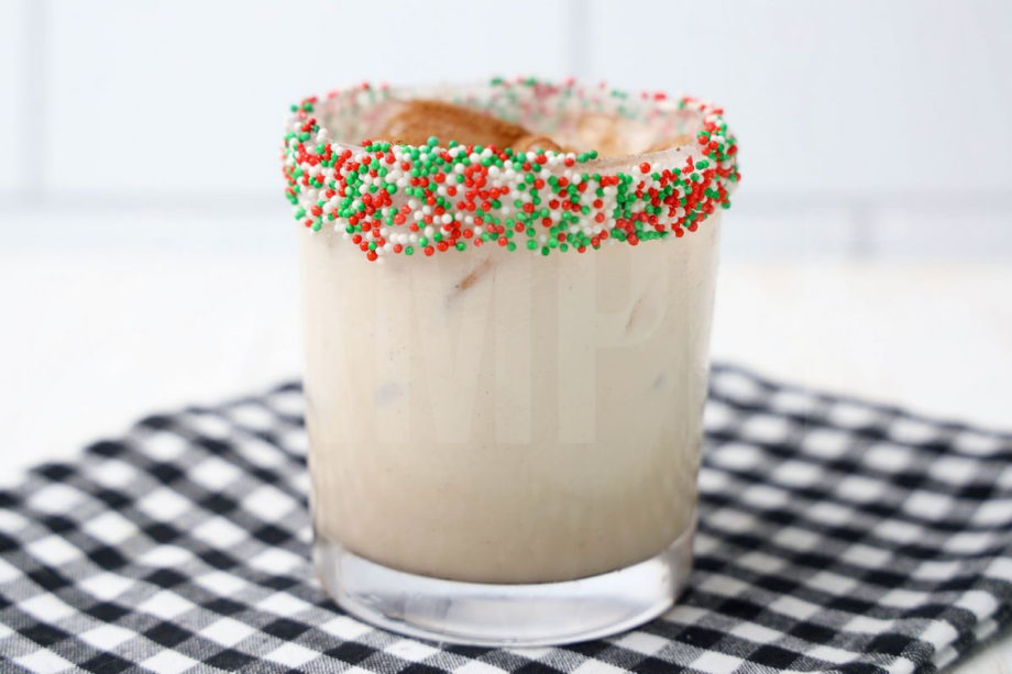 The Gingerbread Cookie Cocktail comes in a glass with a plaid napkin on a white wood backdrop.
