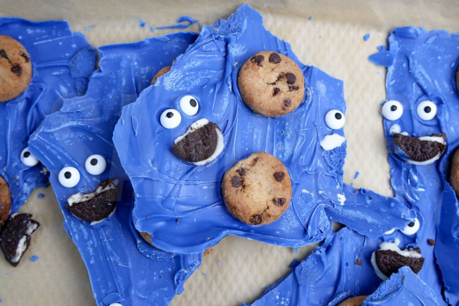 The Cookie Monster Bark comes in a blue pail with parchment paper with a blue and white striped cloth on a white wood backdrop.