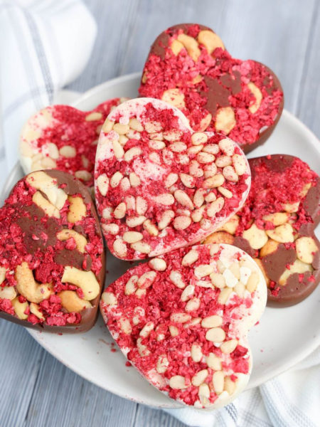 The Heart Raspberry Nut Chocolates comes on a white plate with a light gray and white striped cloth on a gray wood backdrop.