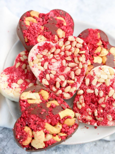 The Heart Raspberry Nut Chocolates comes on a white plate with a white and red heart cloth on a gray wood backdrop.