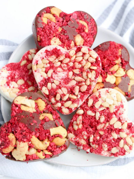 The Heart Raspberry Nut Chocolates comes on a white plate with a thick white and gray striped cloth on a white wood backdrop.