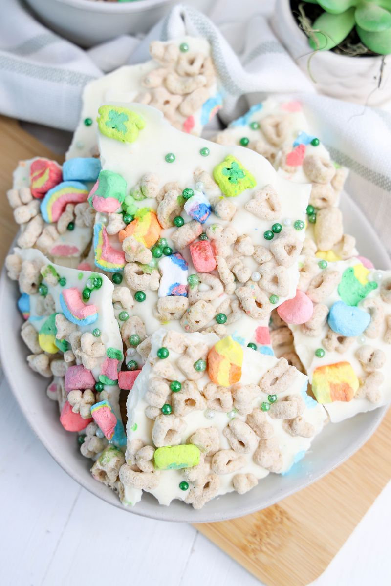 The Lucky Charms Bark comes on a white plate with wood cutting board and green and white striped cloth on white wood backdrop.