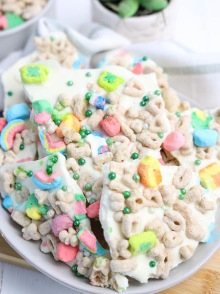 The Lucky Charms Bark comes on a white plate with wood cutting board and green and white striped cloth on white wood backdrop.