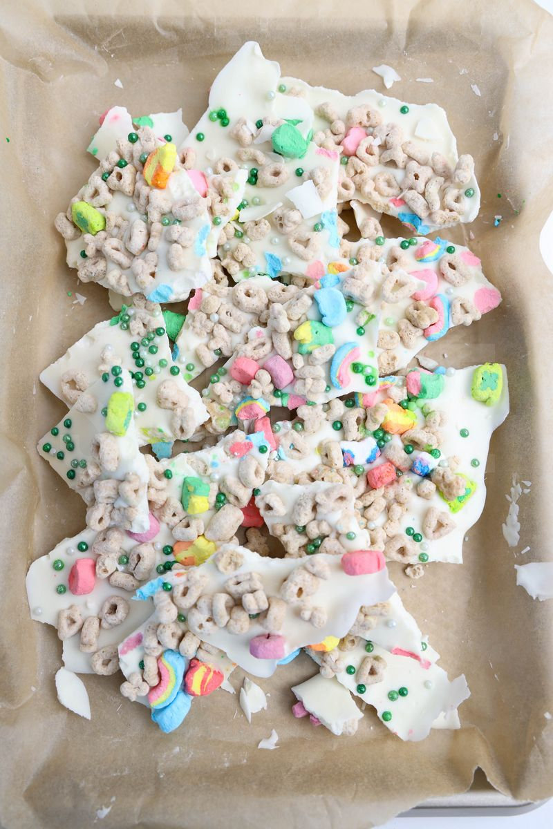 The Lucky Charms Bark comes on a white plate with wood cutting board and green and white striped cloth on white wood backdrop.