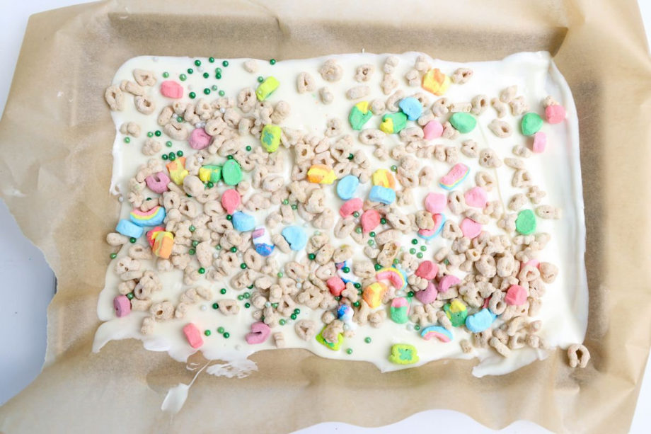 The Lucky Charms Bark comes on a The Lucky Charms Bark comes on a white plate with wood cutting board and green and white striped cloth on white wood backdrop.white plate with wood cutting board and green and white striped cloth on white wood backdrop.