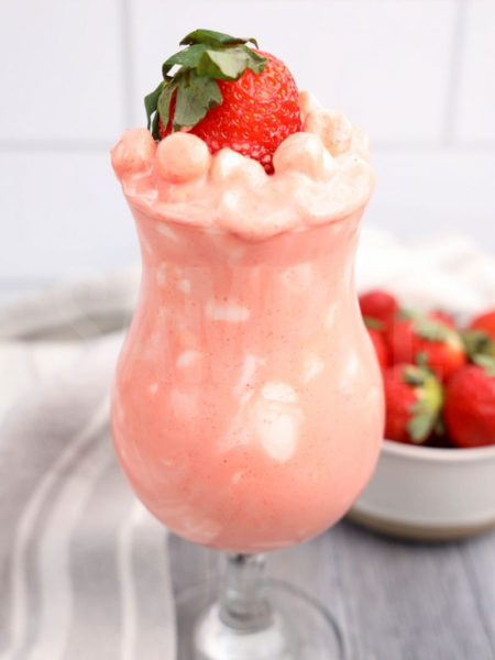 The Strawberry Fluff comes in a clear glass with a white and gray cloth on a gray wood backdrop.