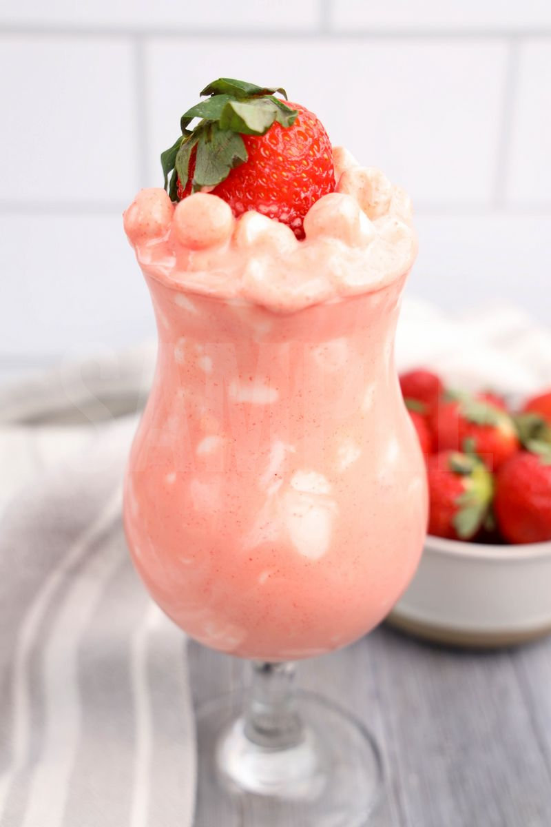 The Strawberry Fluff comes in a clear glass with a white and gray cloth on a gray wood backdrop.