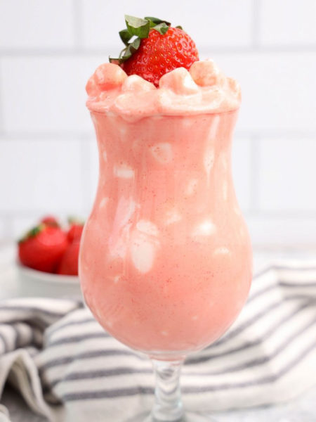 The Strawberry Fluff comes in a clear glass with a white and dark gray cloth on a marble wood backdrop.