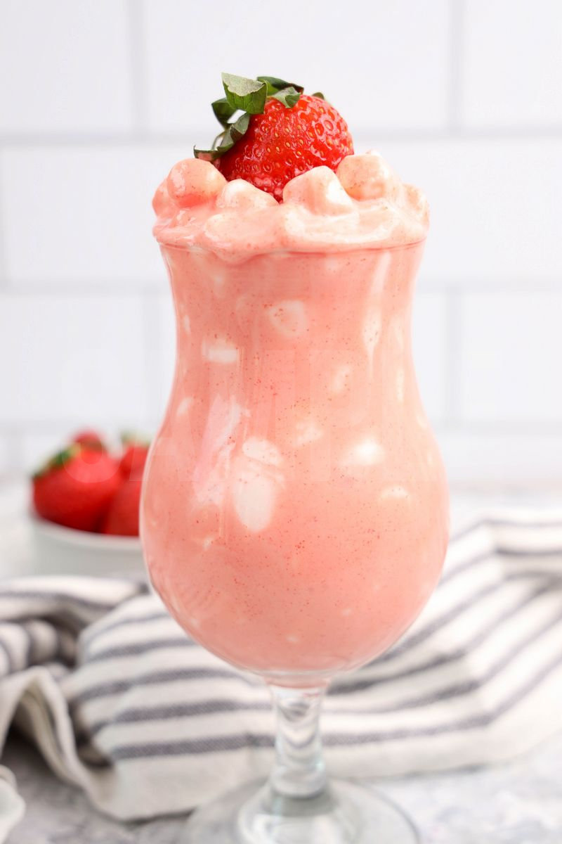 The Strawberry Fluff comes in a clear glass with a white and dark gray cloth on a marble wood backdrop.