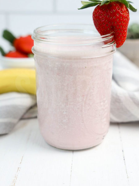 The Strawberry Banana Smoothie comes in a mason jar with a grey and white plaid cloth on white wood backdrop.