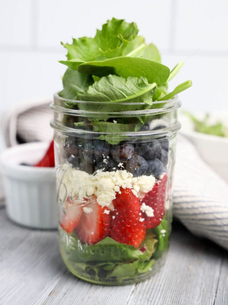 The July 4th Mason Jar Salad comes in a clear glass mason jar with gray wood backdrop.