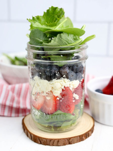 The July 4th Mason Jar Salad comes in a clear glass mason jar with white wood backdrop.